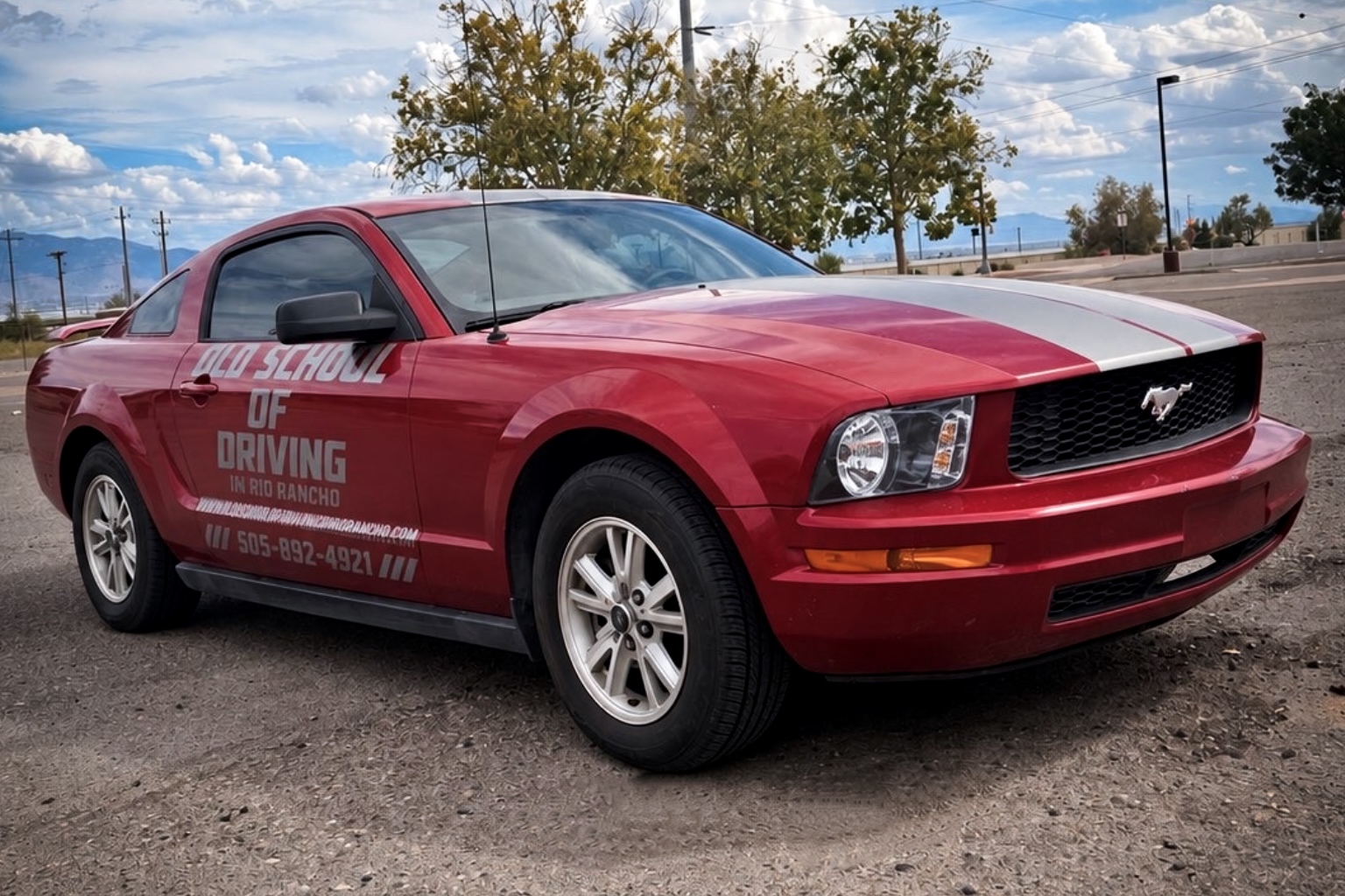 Red Ford Mustang with silver racing stripes and Old School of Driving in Rio Rancho decals parked outdoors